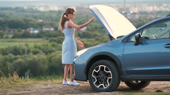 Young Upset Woman Driver Standing Alone Near a Broken Car with Open Hood Inspecting Engine Having