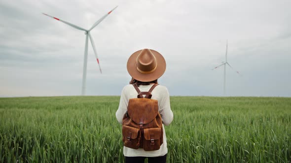 Attractive tourist in a hat and with a backpack in a field with windmills