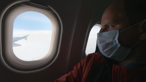 A Man in a Medical Mask Looks Out the Airplane Window