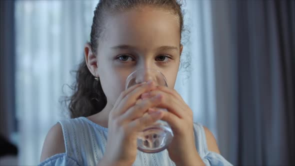 Cute Baby Girl Drinking a Glass of Water Sitting on the Couch at Home. Slow Motion Little Boy