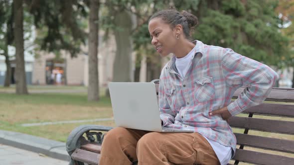 African Woman with Back Pain Using Laptop While Sitting Outdoor on Bench