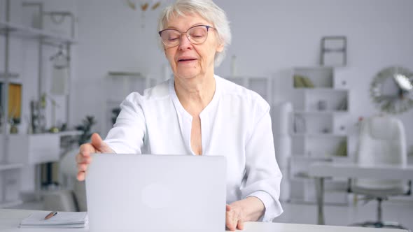Serious aged lady secretary types on laptop then closes computer