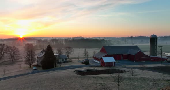 Rural family farm and red barn scene in winter sunrise. Rising aerial establishing shot for agricult