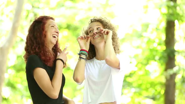 Two girls playing at park and making mustache with their hair