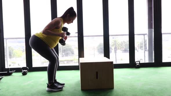 Pregnant female model working out with weights in a gym to keep fit in her fourth trimester