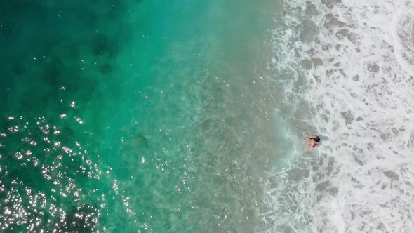 girl enjoying the paradise beach of crystal clear waters on a sunny day. Bird eyes view, pull back
