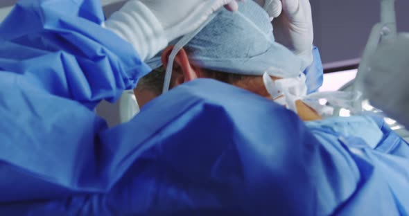 Close-up of female doctor helping male doctor to wear surgical mask in operation theater