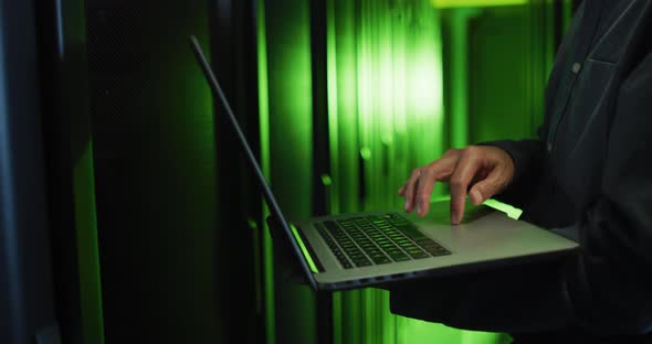 Midsection of asian male it technician using laptop checking computer server