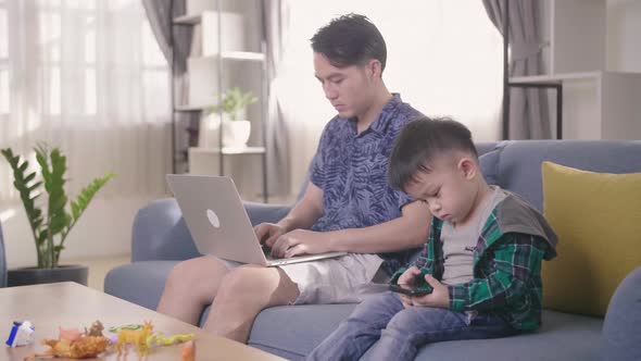 Boring Boy Using Smartphone While Father Working On Laptop
