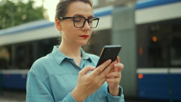 Woman Stands at a Public Transport Stop and Using Smartphone