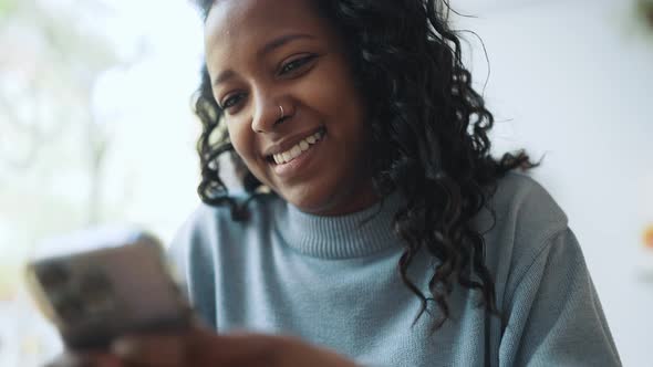 Laughing African woman wearing blue sweater leafing tape on phone