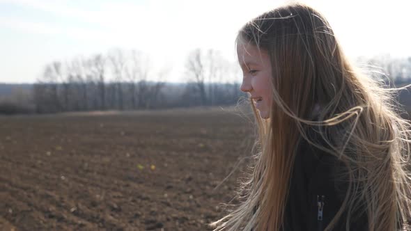 Beautiful Small Girl with Long Blonde Hair Walks on the Dry Ground Through Ploughed Field at Early