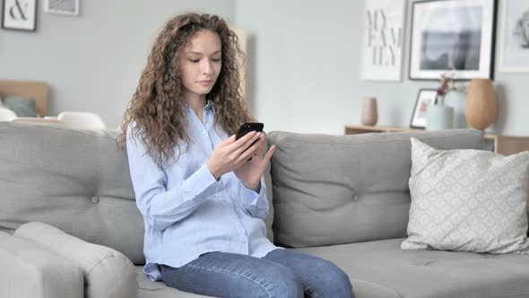 Young Curly Hair Woman Using Smartphone while Relaxing on Sofa