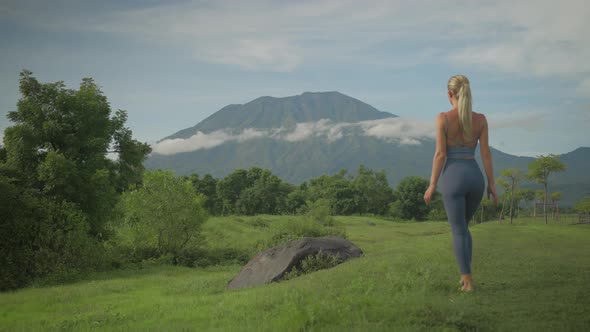 Serene blond woman walking towards boulder to get a better look at volcano Agung