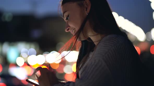 Happy and Smiling Young Woman Using Smartphone at The Evening Time
