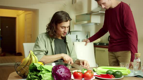 A Young Man Enters Into a Kitchen While His Friend is Cooking a Salad