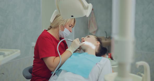 Female Dentist Gently Drills a Tooth to a Patient Working with a Boron Machine