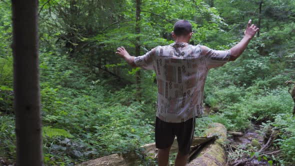 Young man balancing barefoot on an slippery fallen tree in a wild beautiful forrest with a little ri