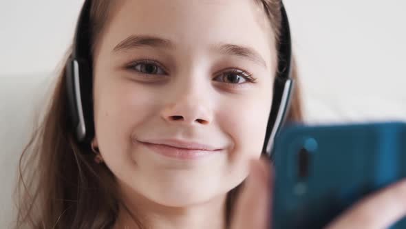 Cute Girl Enjoying Music with Headphones at Home Looking at the Camera and Smiling Closeup