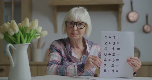 Senior Teacher in Glasses Showing Sheet of Paper with Simple Mathematical Equations Looking 