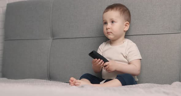 The Little Boy Sits on the Bed and Watching TV