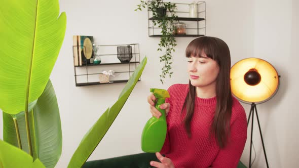 Smiling Caucasian Woman with Dark Long Hair Holding Cleaning Tools in Living Room Next to Plant