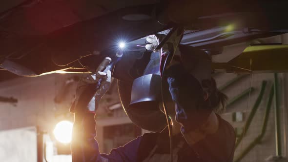 Female mechanic wearing welding helmet welding under a car at a car service station