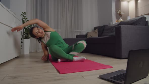 Sporty Woman Doing Stretching Workout Looking at Laptop Indoors