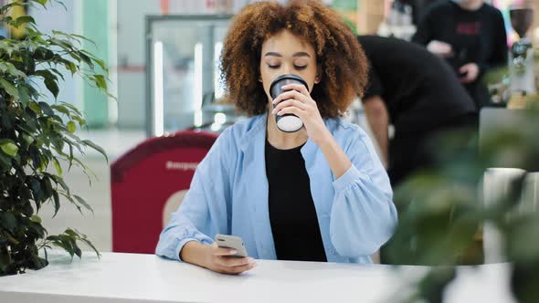 African 20s Woman Multiracial Biracial Lady with Curly Haircut Sitting at Cafe Table Drinking Coffee