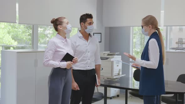 Mature Female Real Estate Agent in Safety Mask Showing Office Interior to Business Couple