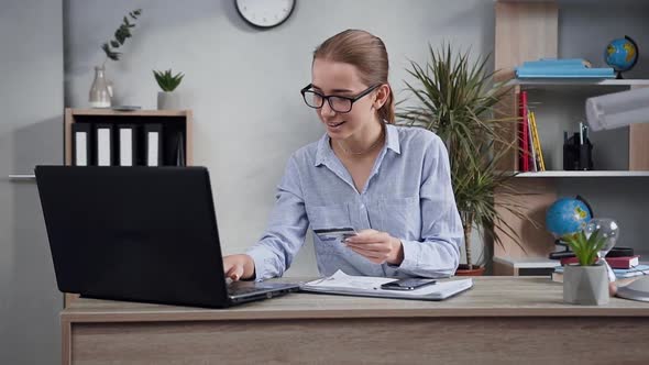 Young Woman Using Computer and Her Bank Card to Make Online Payment for Purchase