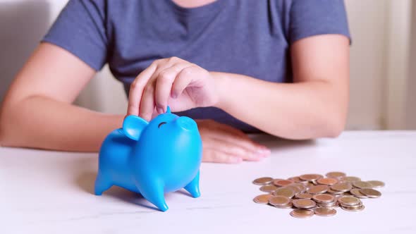 Woman's hand putting coins into blue piggy bank. Finance concept