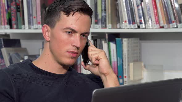 Handsome Man Talking on the Phone, While Doing Homework on Laptop