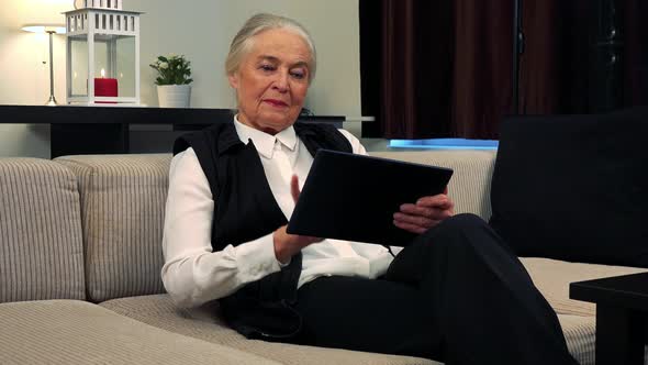 Old Caucasian Woman Works on Tablet in Living Room