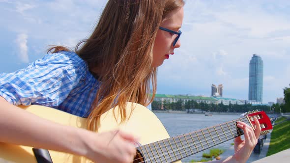 A Woman Is Playing the Acoustic Guitar Outdoors