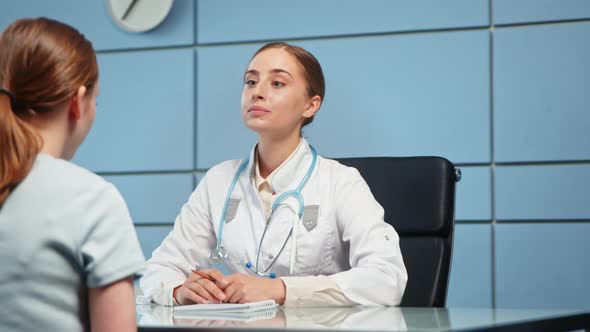 Young woman doctor in white coat examines hospital visitor