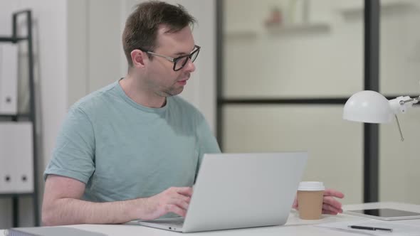 Young Man Drinking Coffee While Typing on Laptop