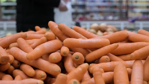 Carrots by weight against the background of a man who picks vegetables in a plastic bag