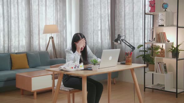 Asian Female Footwear Designer Having A Headache While Working On A Laptop At Home