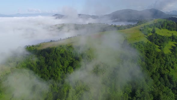 Aerial Shot. Flying Through the Clouds Over Green Hills Covered with Grass and Trees. Morning Lower