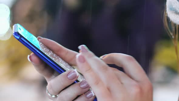 Closeup of a Woman's Hand Uses the Mobile Phone App in the Snowy Evening, Christmas and New Year