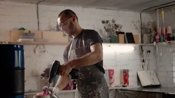 A male handyman mixes paint in a can in a workshop. A sculptor mixes resin with paint to a vase.