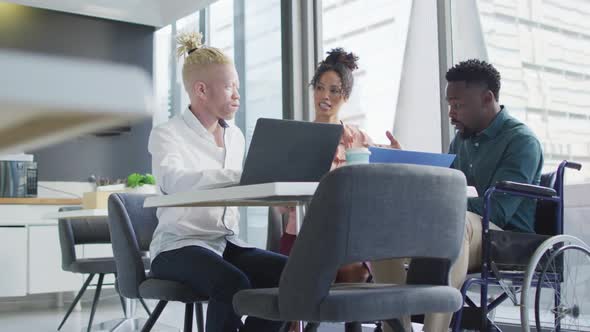 Diverse business people discussing with disabled colleague and documents in creative office