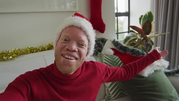 Happy albino african american man wearing santa hat making video call at christmas