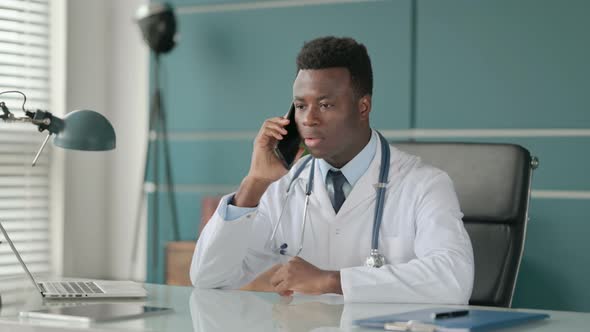 African Doctor Talking on Smartphone While Working on Laptop