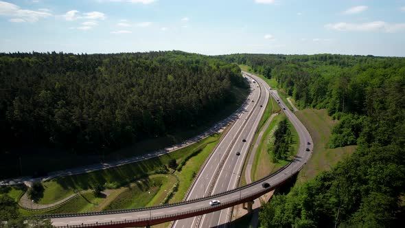 Ascending aerial view of cars driving on new asphalt route surrounded by forest in summer - 4K Drone