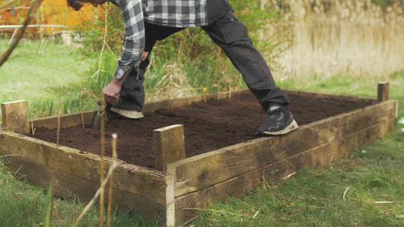 Young man using trowel making row for sowing seeds raised garden bed