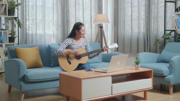 Smiling Asian Woman With Laptop Enjoy Playing Guitar At Home