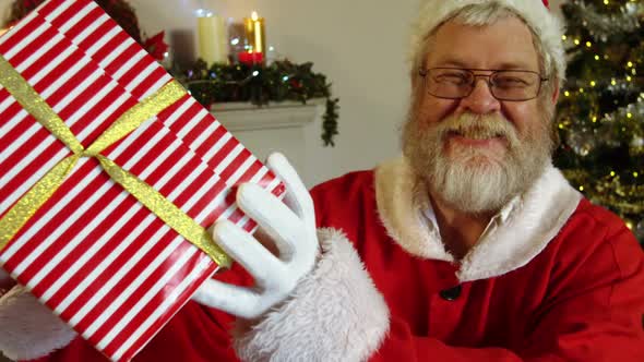 Portrait of santa claus holding gift box with finger on lips