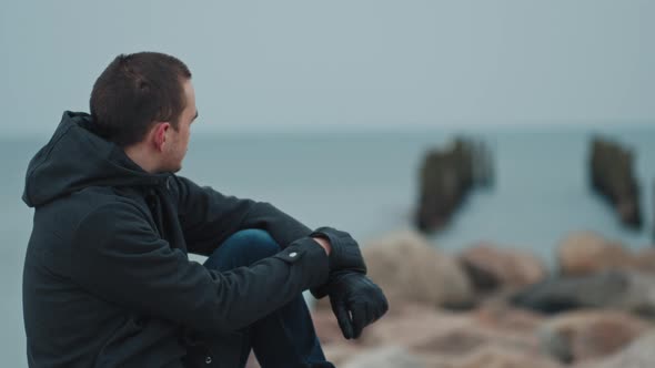 young guy sits on a stone against the backdrop of the blue sea